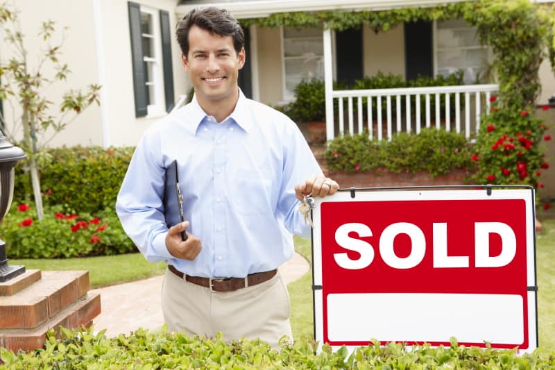 Real estate agent standing in front of a house and beside of a sold sign