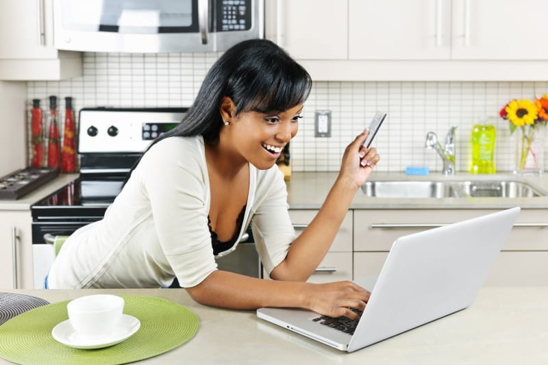 Smiling woman shopping online with a laptop computer and credit card in the kitchen
