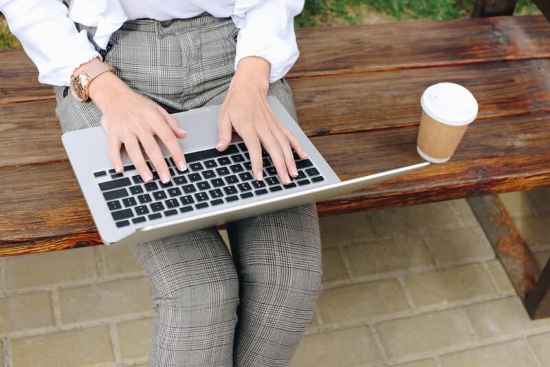 Woman sitting on a bench typing on a laptop computer