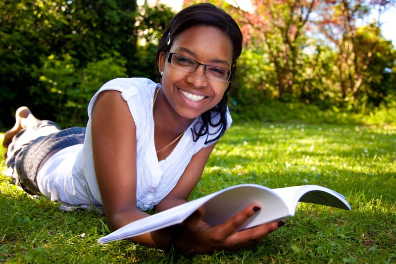 Smiling young woman lying in the grass on a sunny day reading.
