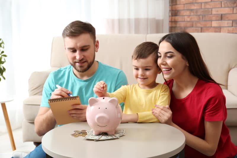 Man and woman with young boy putting money in a piggy bank.